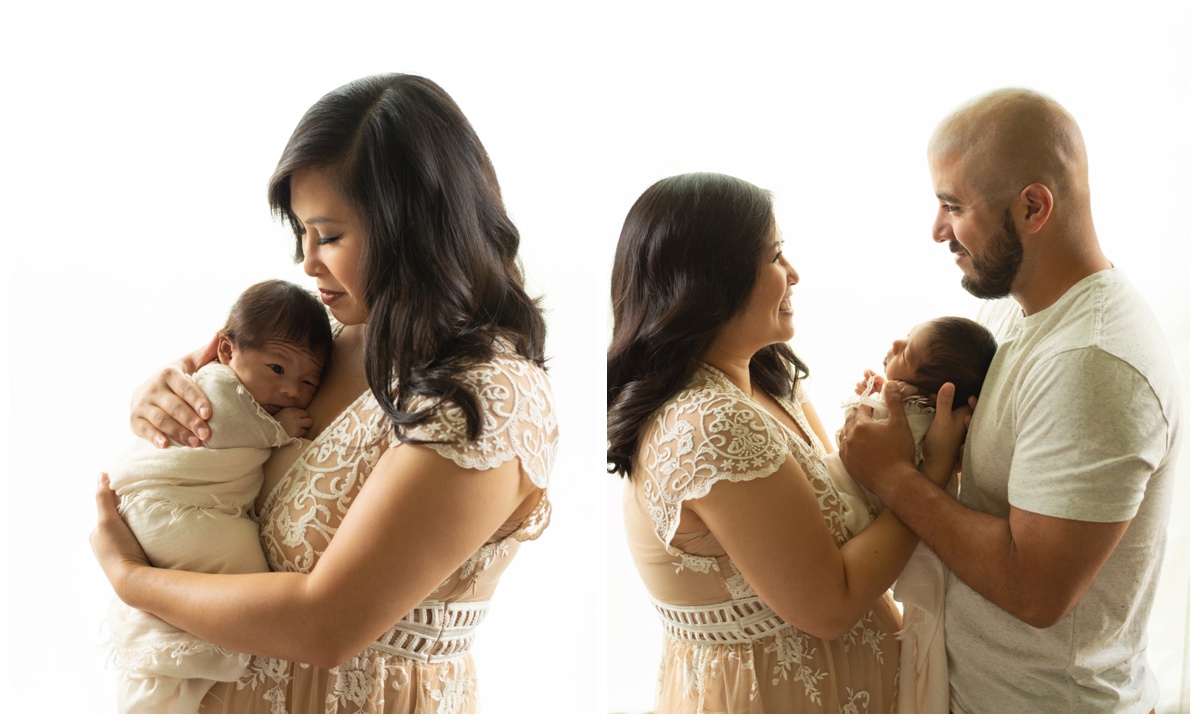 Mother in lace dress smiling at newborn and husband in a Houston photo studio