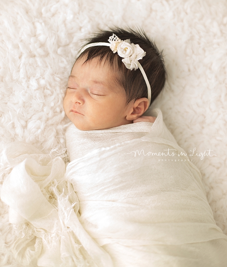 A baby girl with lots of black hair sleeps while swaddled. 