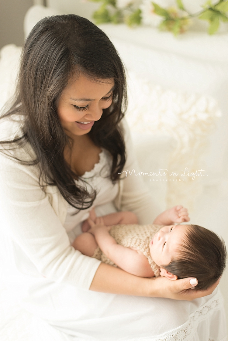 A mother with long black hair smiles at her new baby on her lap. 