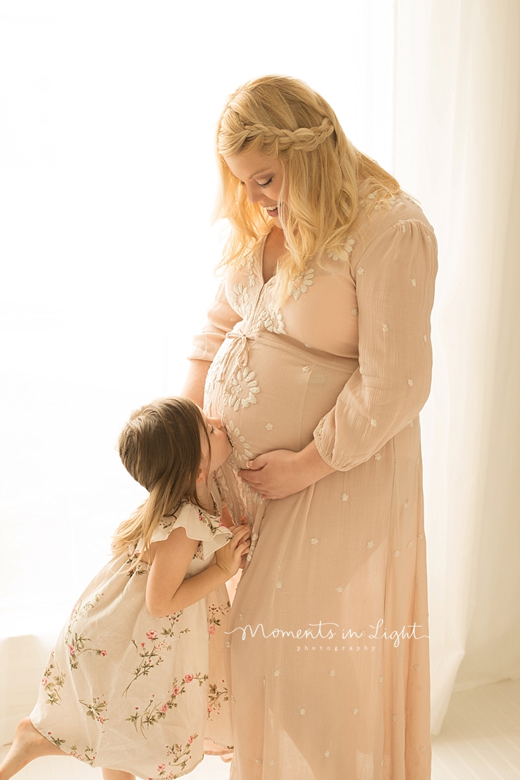 A little girl kisses her moms growing belly. 