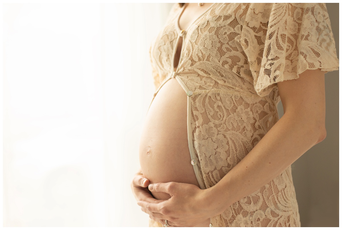 A woman's bare belly in a beige lace dress by maternity photographer in The Woodlands