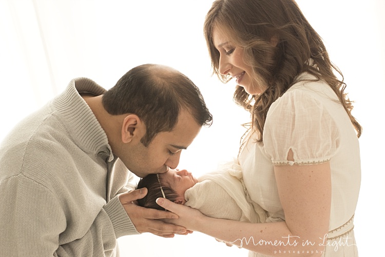 A man leans down to kiss his baby girl newborn. 