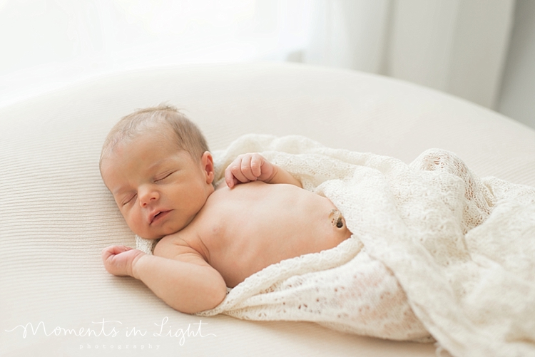 A newborn's belly button is exposed as the blanket falls off of her. 