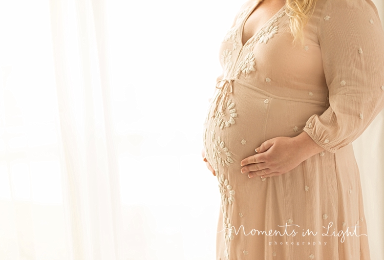 A pregnant woman stands by a window. 