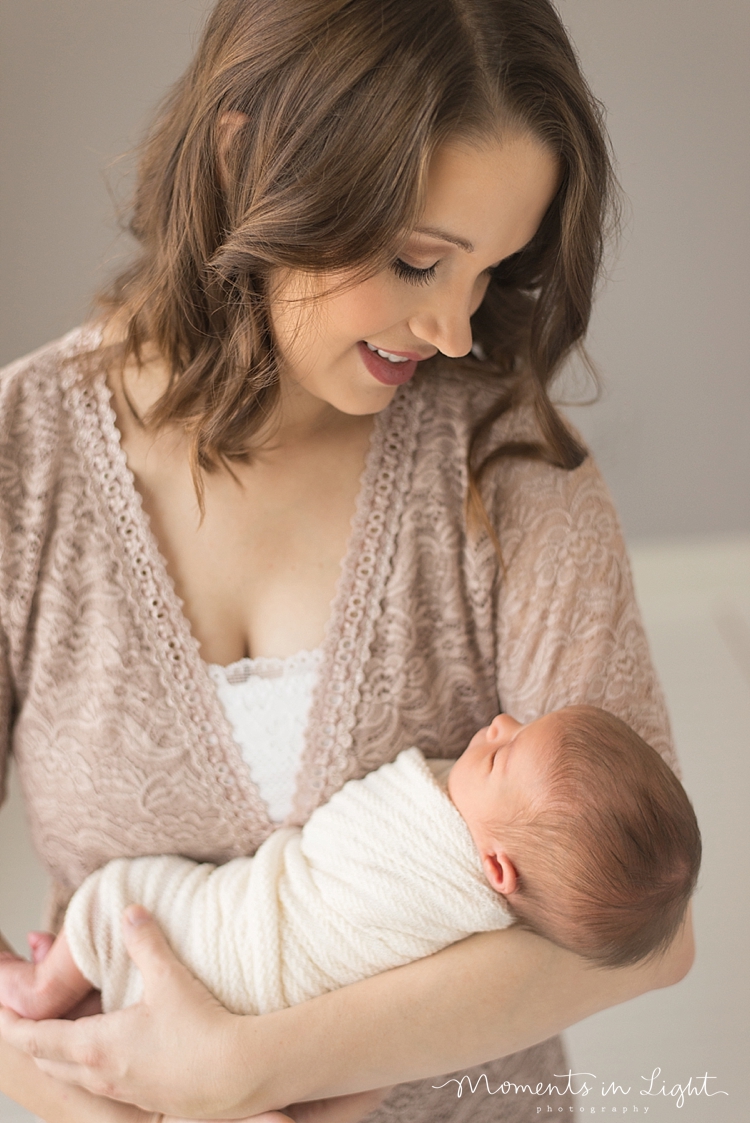 A mother looks down at her newborn during their family with newborn photography session. 