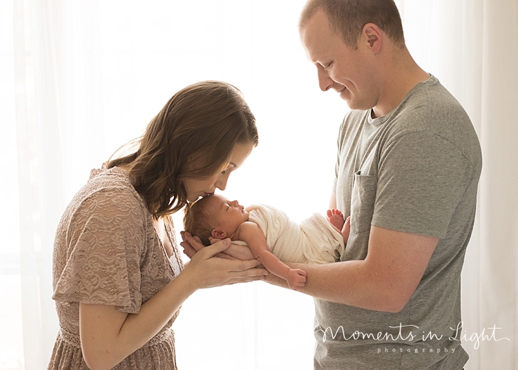 A mother bends over to kiss her newborn on the head. 