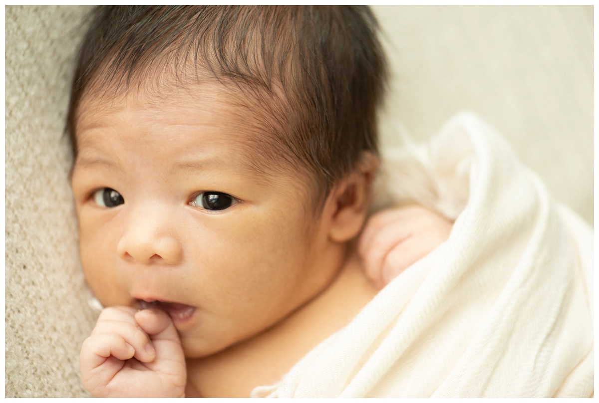 Swaddled newborn baby with hand in mouth in a Montgomery, Texas photo studio