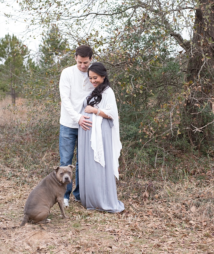 A couple stands behind their dog. 