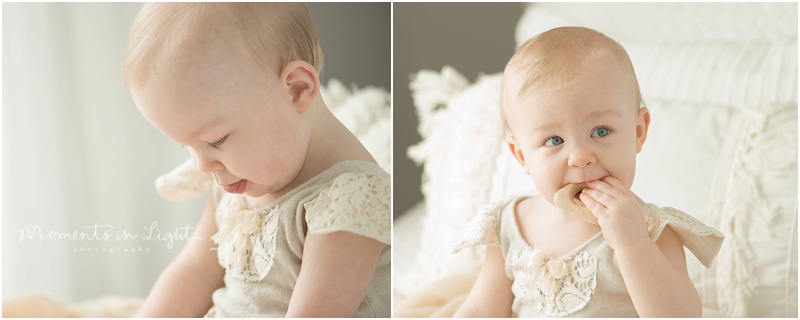 A baby chews on a toy as she sits for her twin first birthday photos.