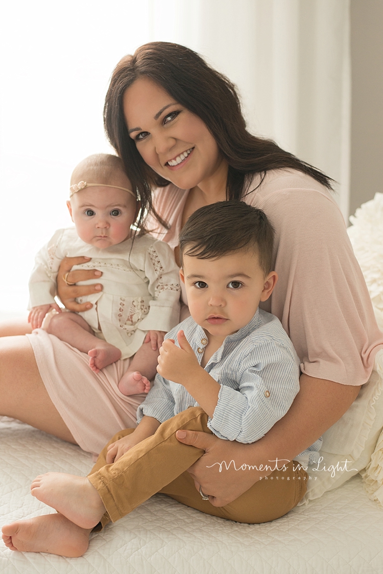 A baby photographer captures a mom holding her babies in her lap. 