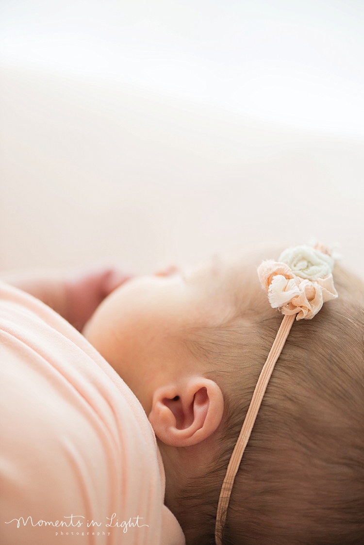 A newborn wears a floral headband on her head while she naps. 