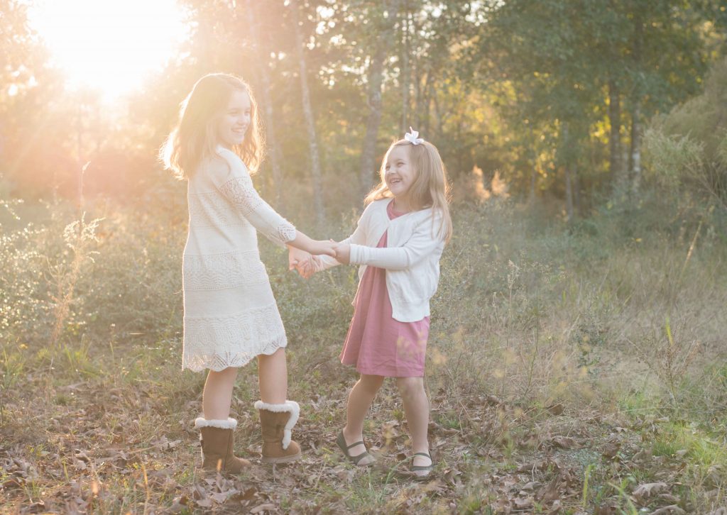 two little girls holding hands and smiling at sunset in a field in The Woodlands, TX