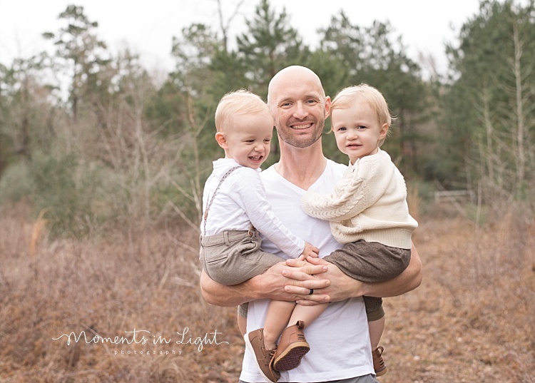 A father smiles as he holds his twin baby boys. 