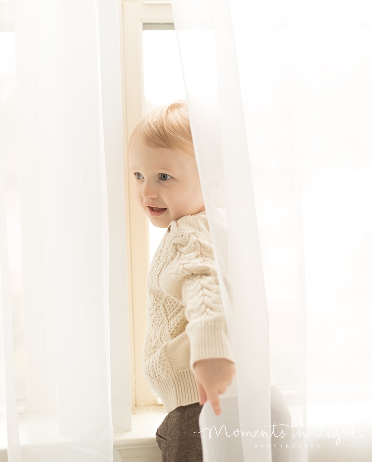 A little boy plays in the curtains. 