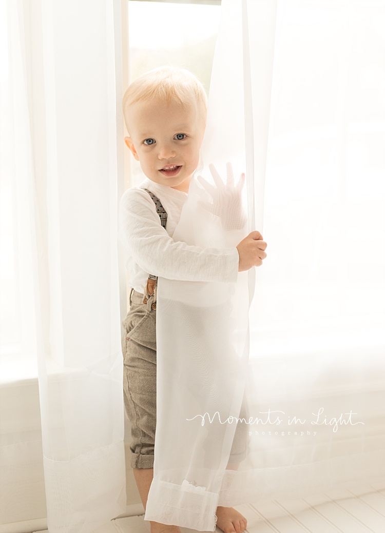 A little boy plays in some white curtains. 