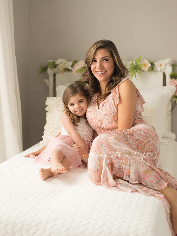 A baby and child photographer captures a mother cuddling her child on a bed. 