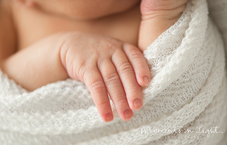 A baby's hand grasps the blanket she's wrapped in. 