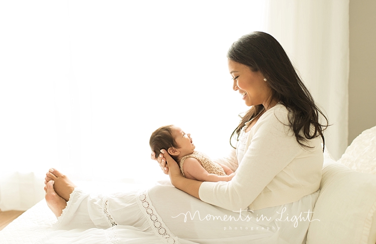 A woman wearing a white dress holds her newborn on her lap. 