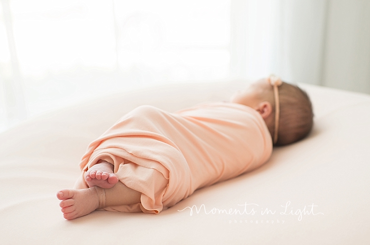 A newborn girl sleeps on a white surface while swaddled in pink. 