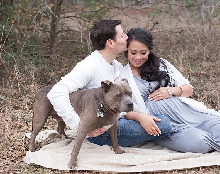 A couple sits on a blanket with their dog. 