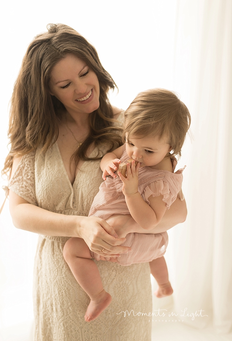 A baby sucks her thumb while her mother holds her on her hip. 