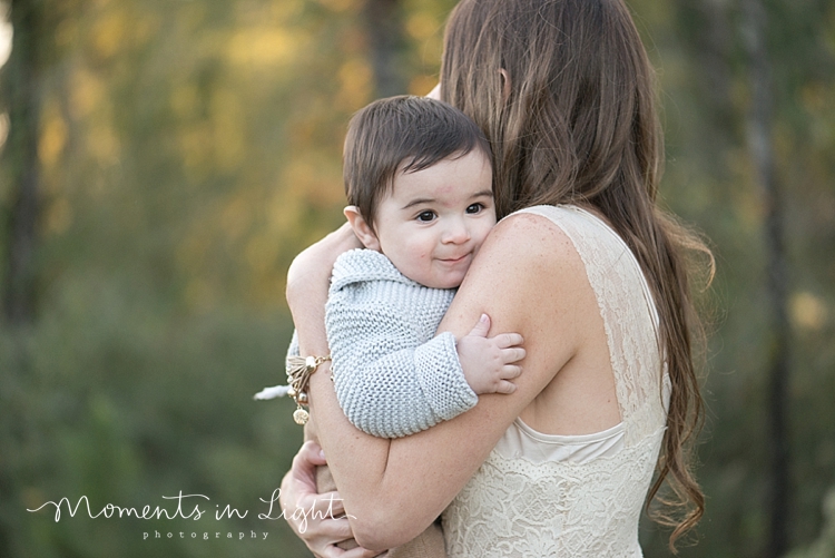 Baby boy looking over his mother's shoulder in a field by Houston family photographer