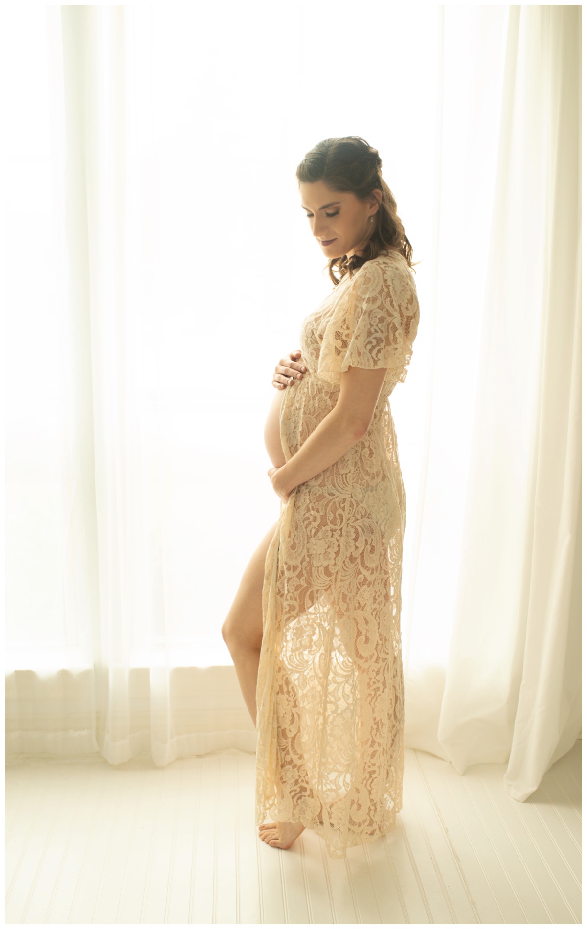 Side-view of expectant mother in lace dress standing in window of Houston maternity photo studio