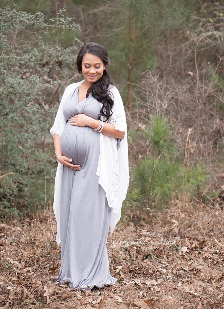 A pregnant woman stands in front of some tall grass. 