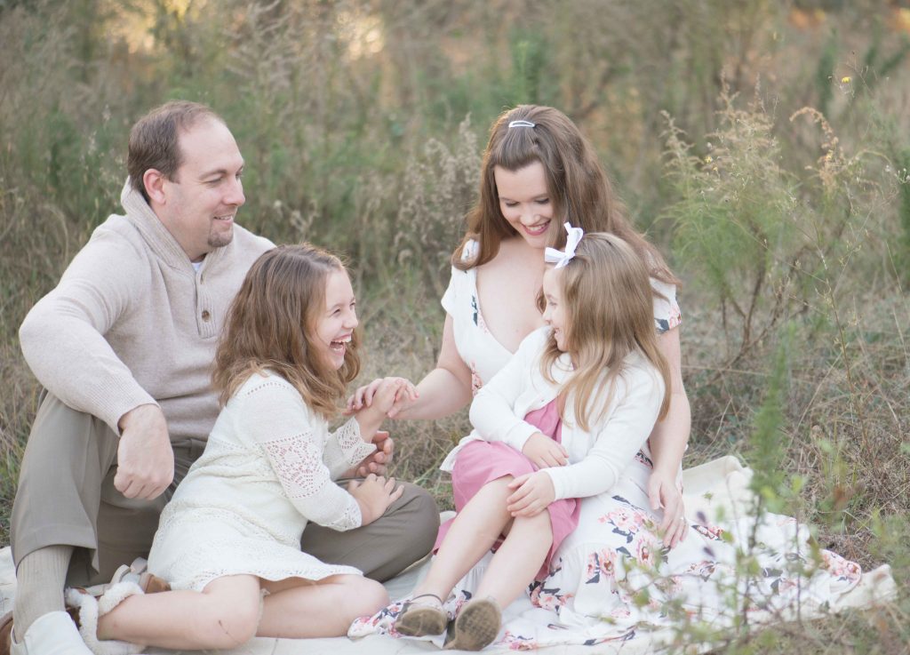 family with two little girls laughing in a field in the Woodlands, TX