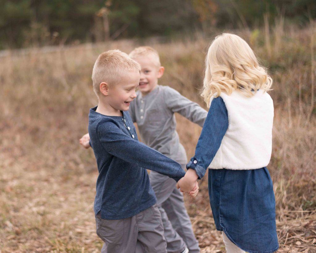 triplet brothers and sisters holding hands and spinning in a circle in Montgomery, TX