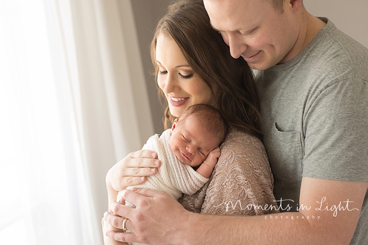 Moments In Light Photography captures parents hugging their newborn while she sleeps. 