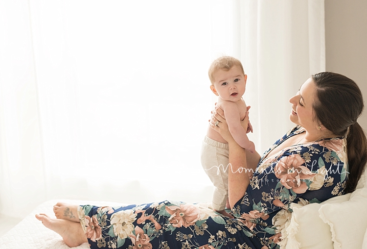 A mother holds her baby on her lap during a baby photography session by Moments In Light Photography. 