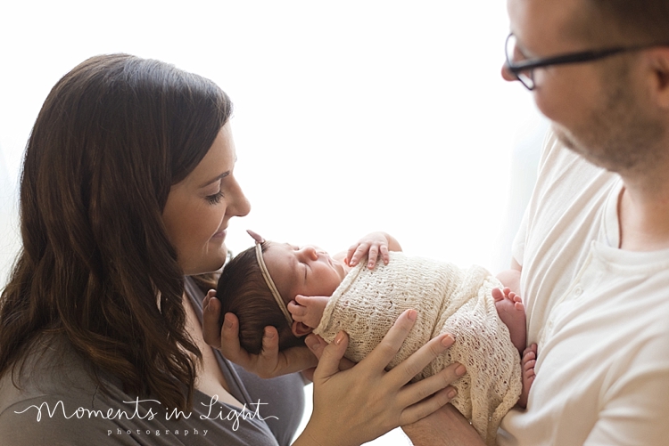 Mother and father smiling down at swaddled baby daughter in Houston newborn photography studio