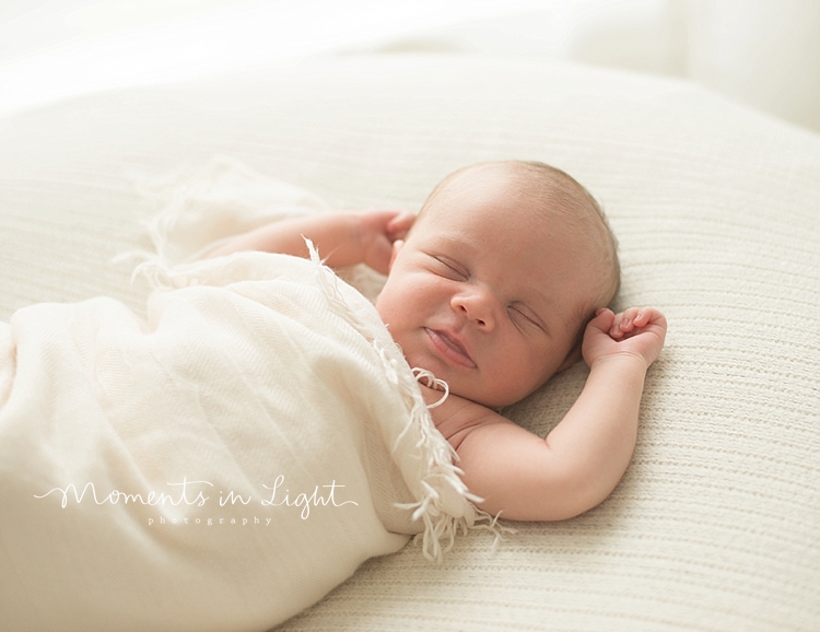 A baby smiles in her sleep during a newborn baby photography session with Moments In Light Photography. 