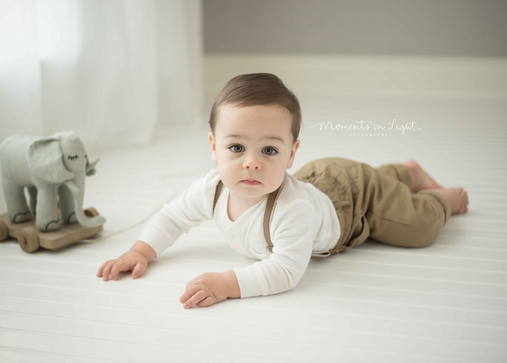 one year old baby boy with brown eyes laying on stomach by window light with toy elephant