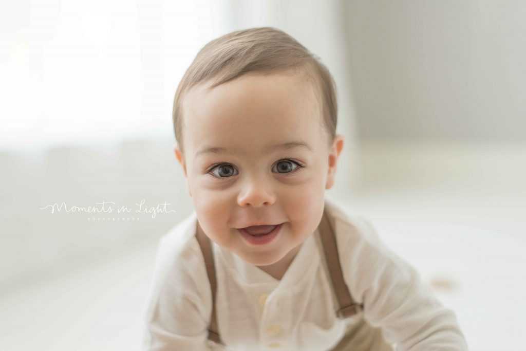 little boy smiling wearing suspenders by window light