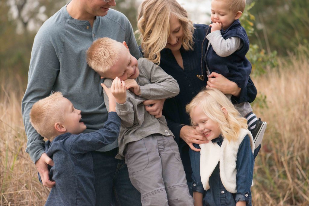 mom and dad with 4 small children laughing and hugging in a field in Montgomery, TX