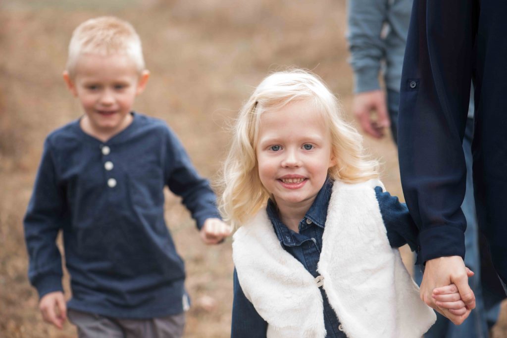 little girl holding mom's hand with her brother running behind them 