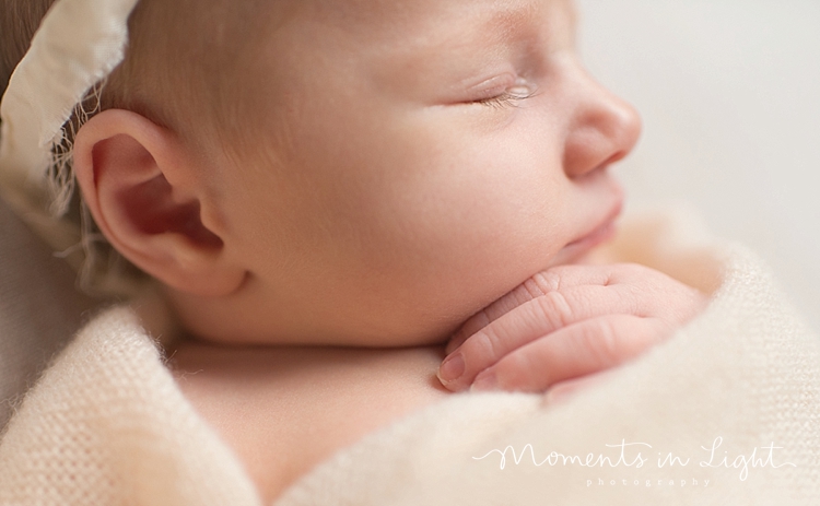 A baby is sleeping with her hand on her chest during a session with Moments In Light Photography. 