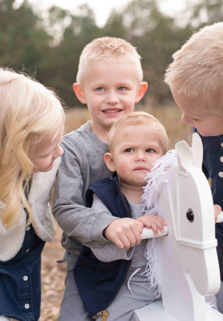 baby boy on a rocking horse with brother and sister helping in a field in Montgomery, TX