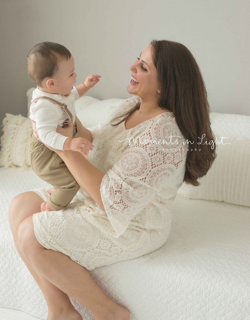 mom smiling and holding baby boy on white couch in The Woodlands, TX