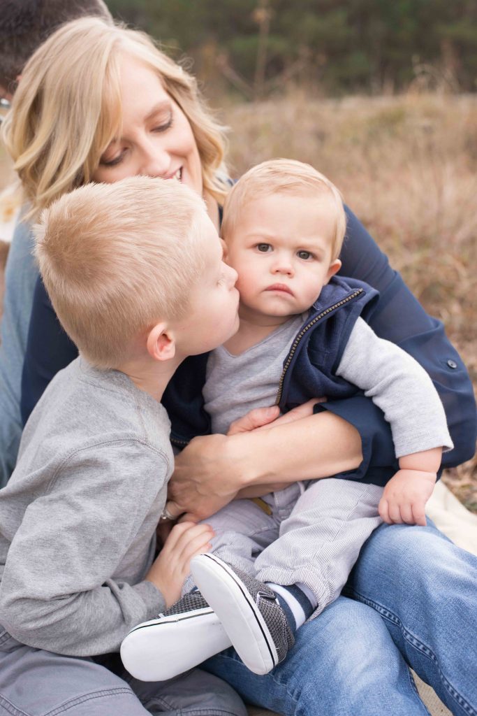 mom holding baby boy while big brother gives him a kiss