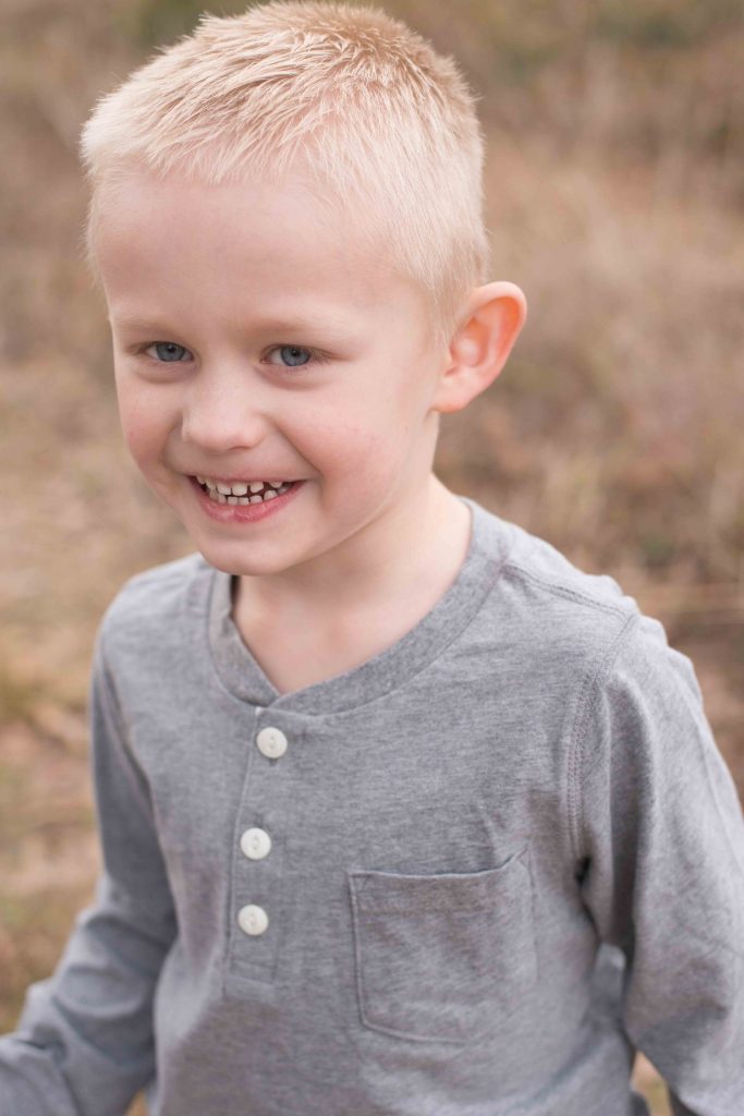 blonde little boy with blue eyes smiling in a field in Montgomery, TX