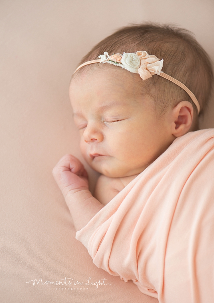 Moments In Light Photography captures a newborn sleeping with her hand by her face. 