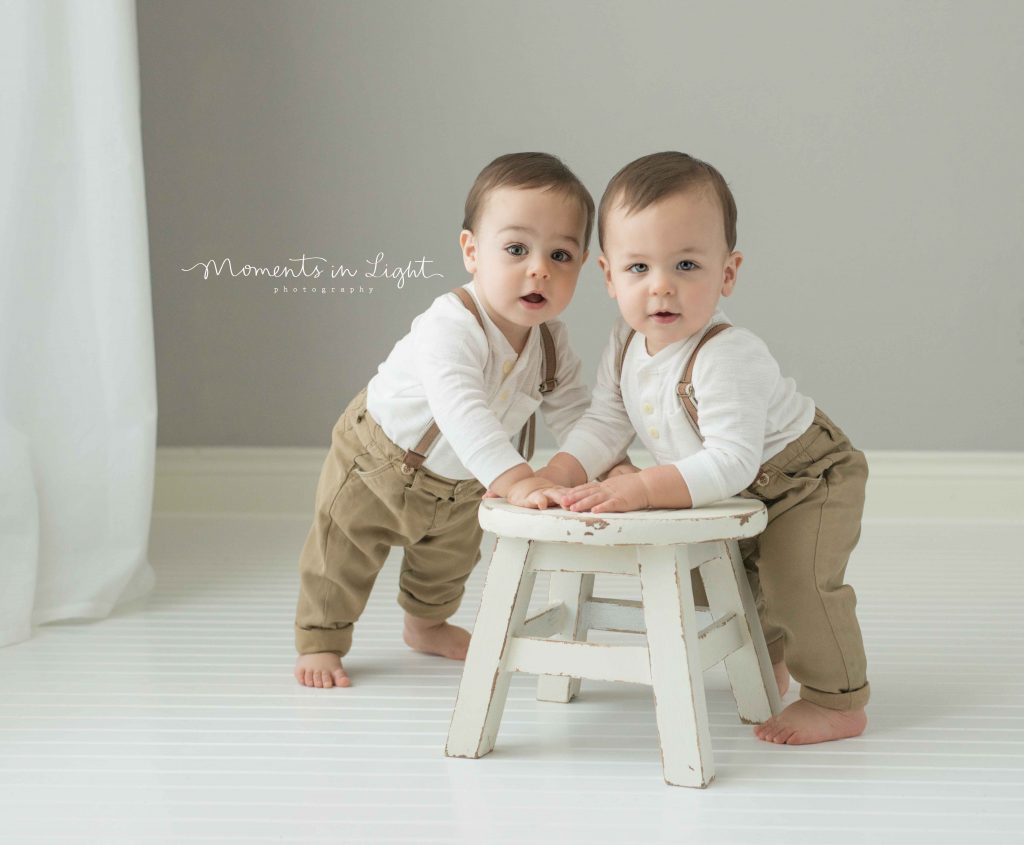 one year old twin boys smiling at camera holding on to white still in photo studio in Montgomery, TX