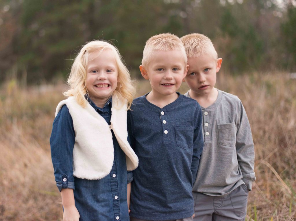 triplet brothers and sister smiling in a field in Montgomery, TX