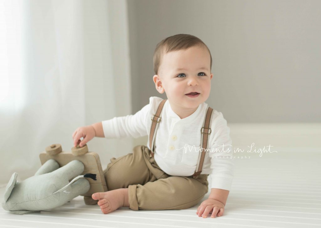 one year old boy smiling playing with elephant toy in photo studio in The Woodlands, TX