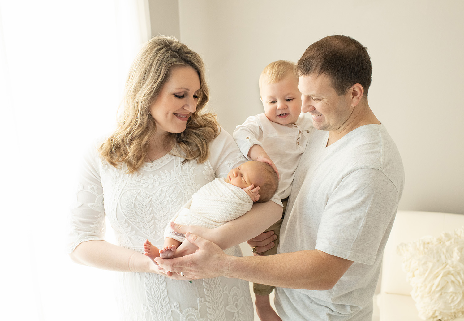 Family newborn picture with parents and sibling touching baby 